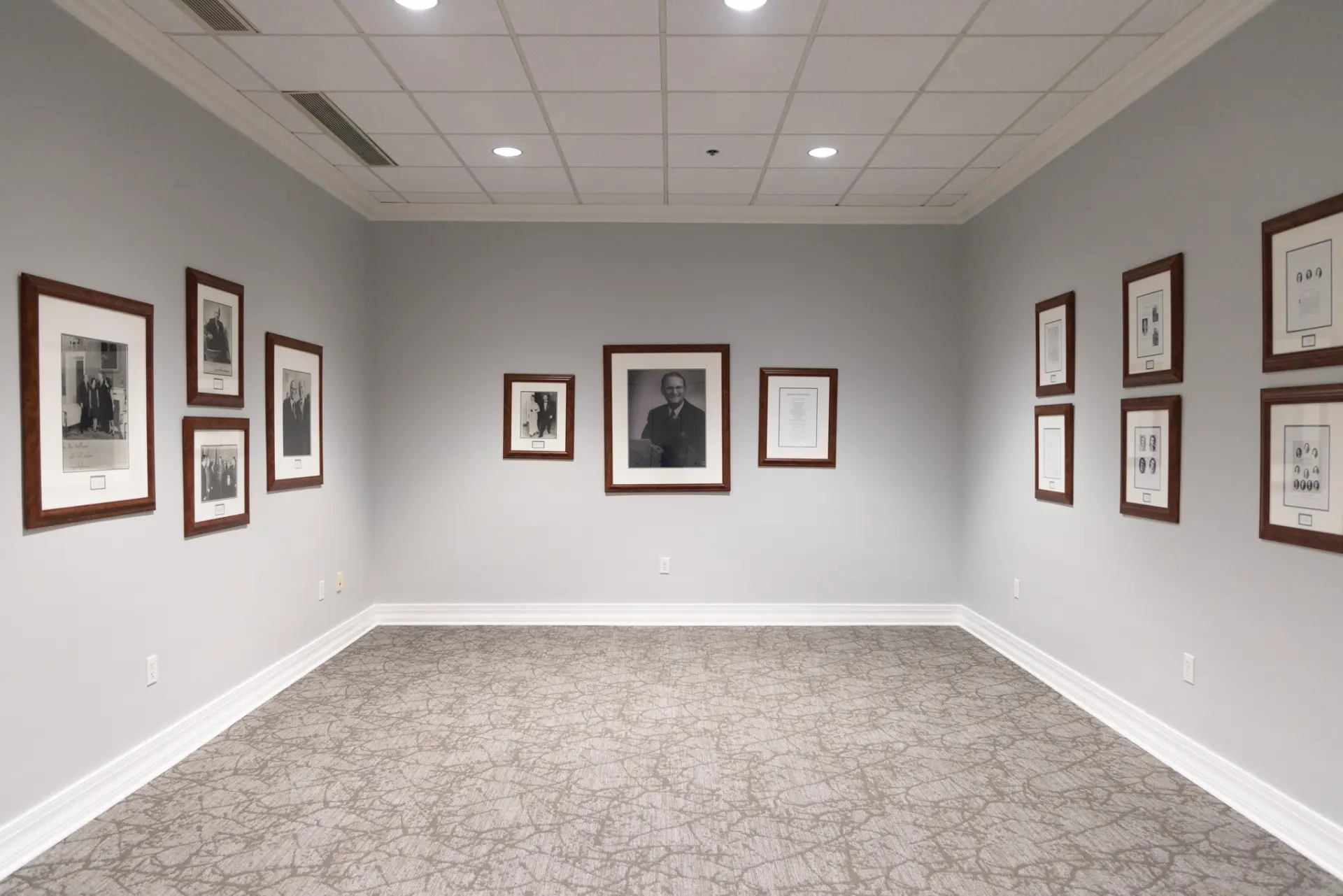 Empty room with framed pictures on the walls, white ceiling, and gray carpet.