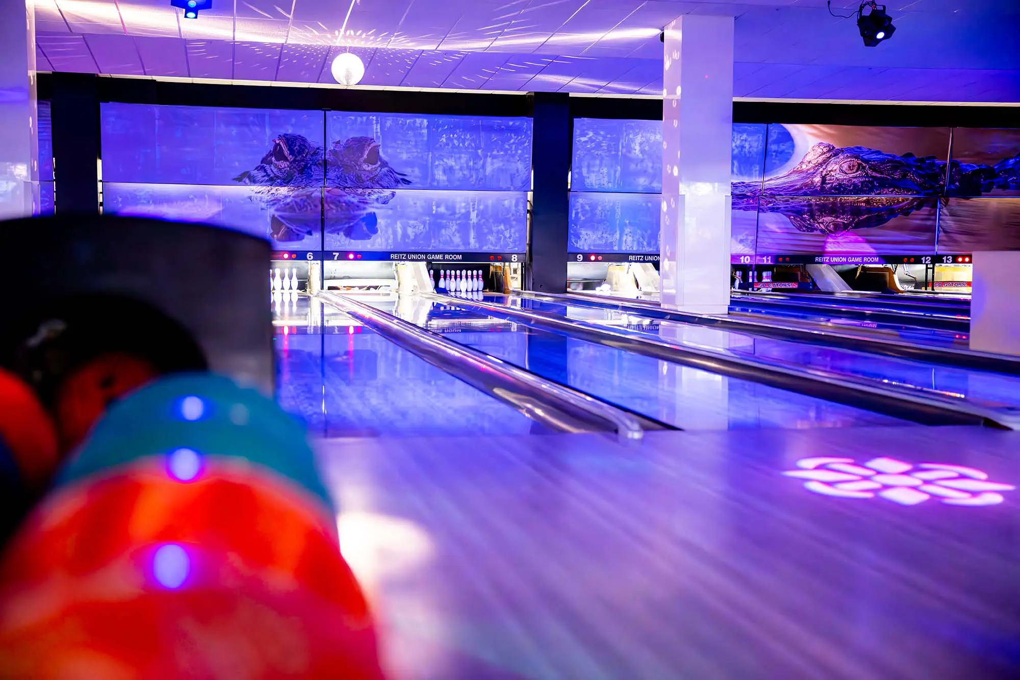 A bowling lane with a colorful ball in the foreground and a large screen displaying a bowling alley in the background.