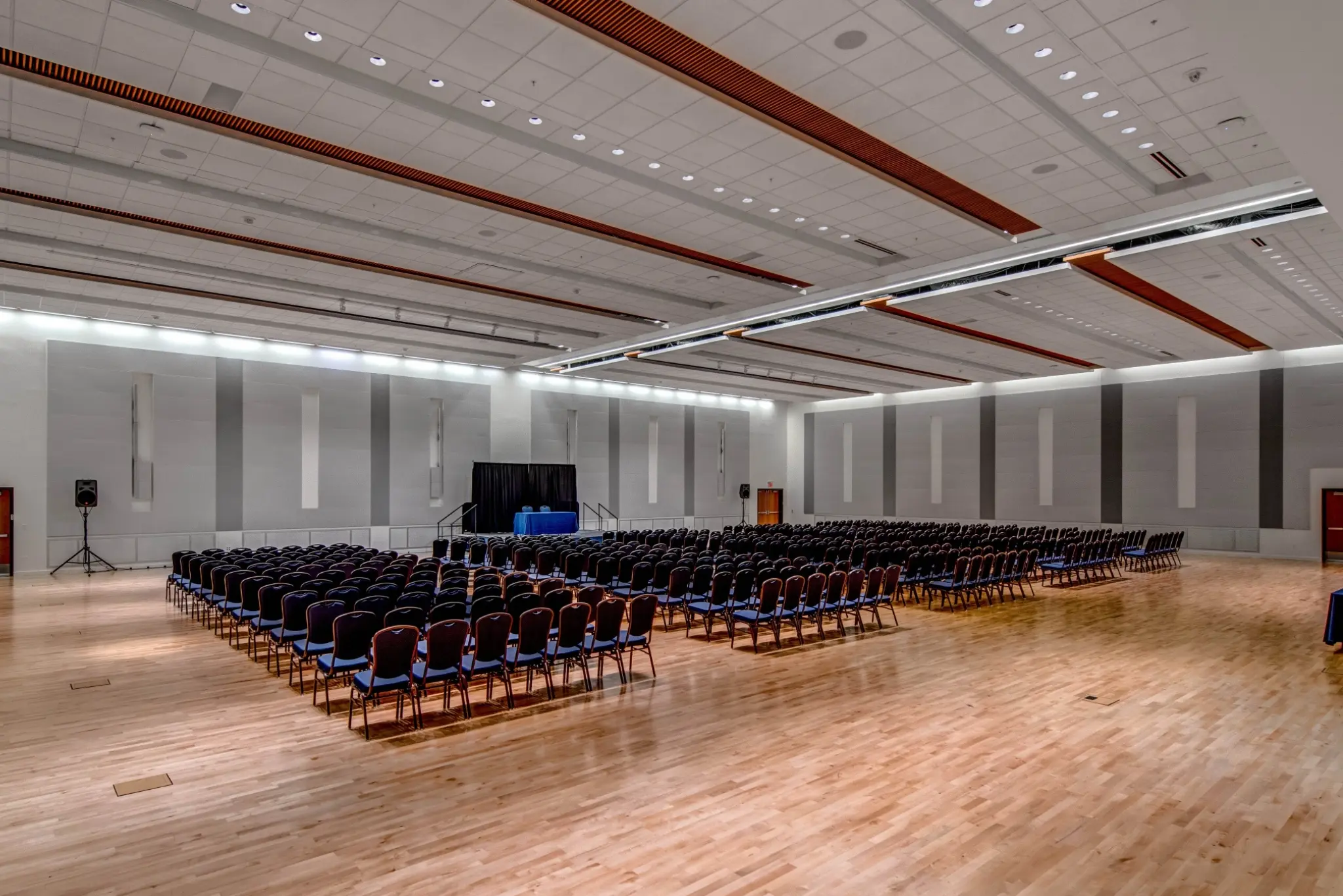 A large room with rows of chairs, wooden floor, and white walls, possibly for a conference or event.