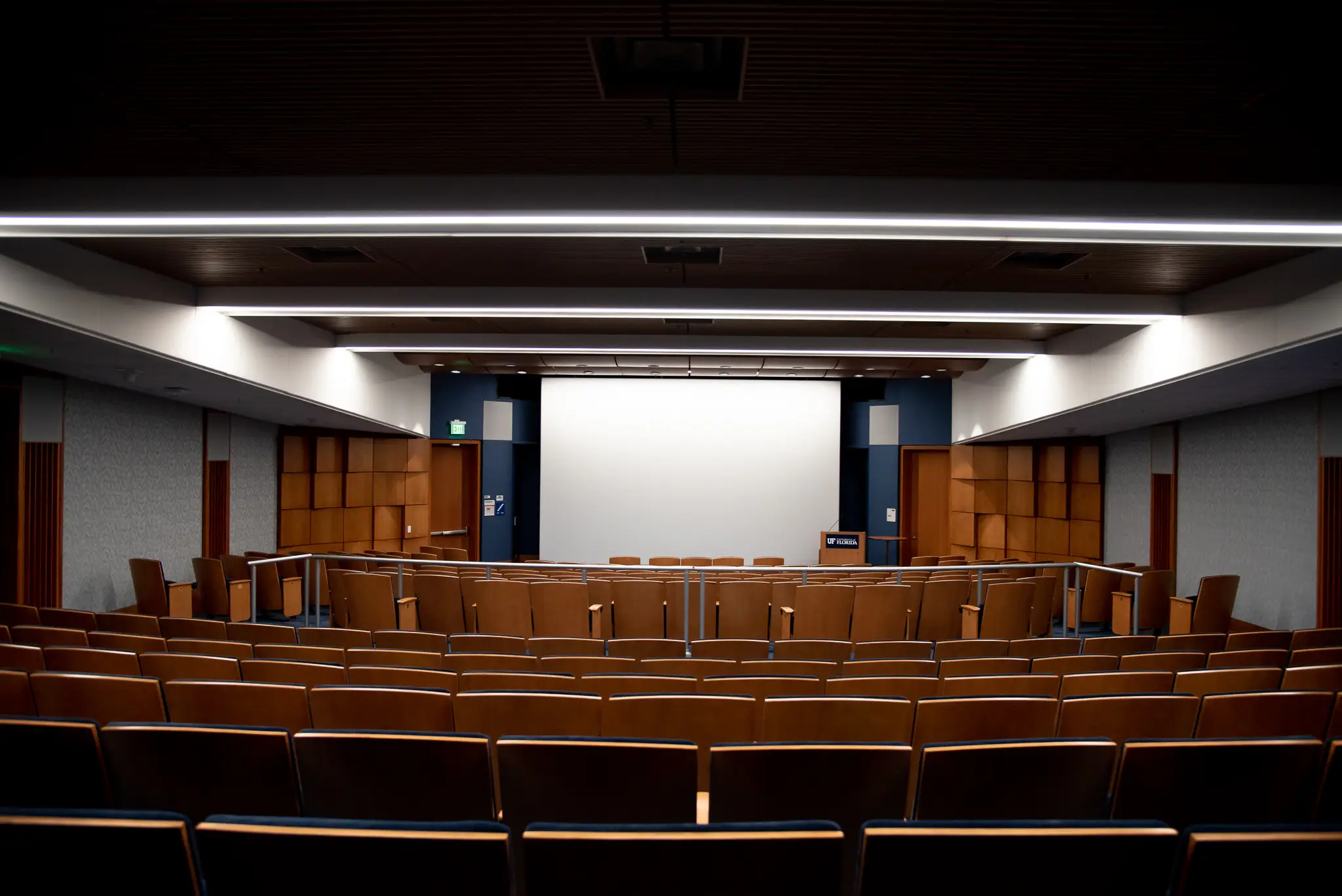 Empty courtroom with wooden chairs, podium, and screen.