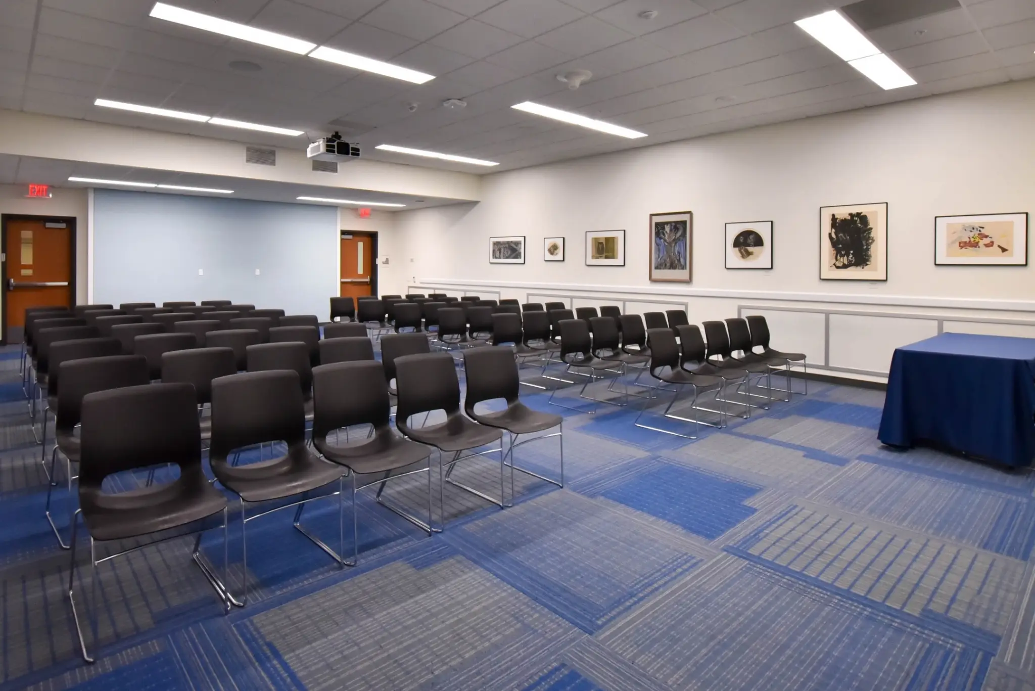 A room with a projector screen, chairs, and artwork on the wall.