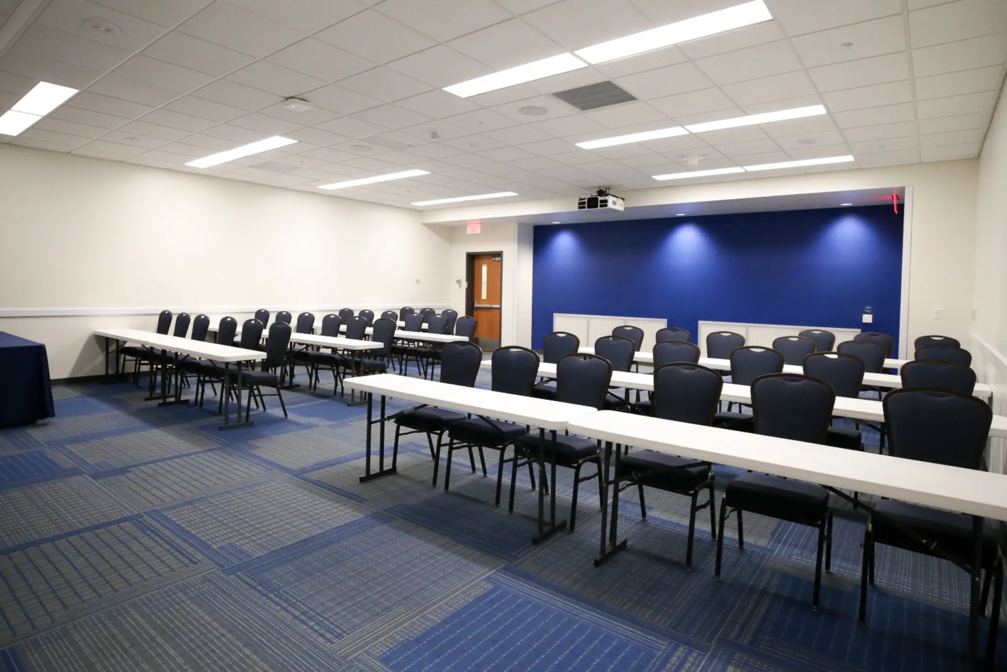 A long conference table with chairs in a room with blue carpeting and white walls.