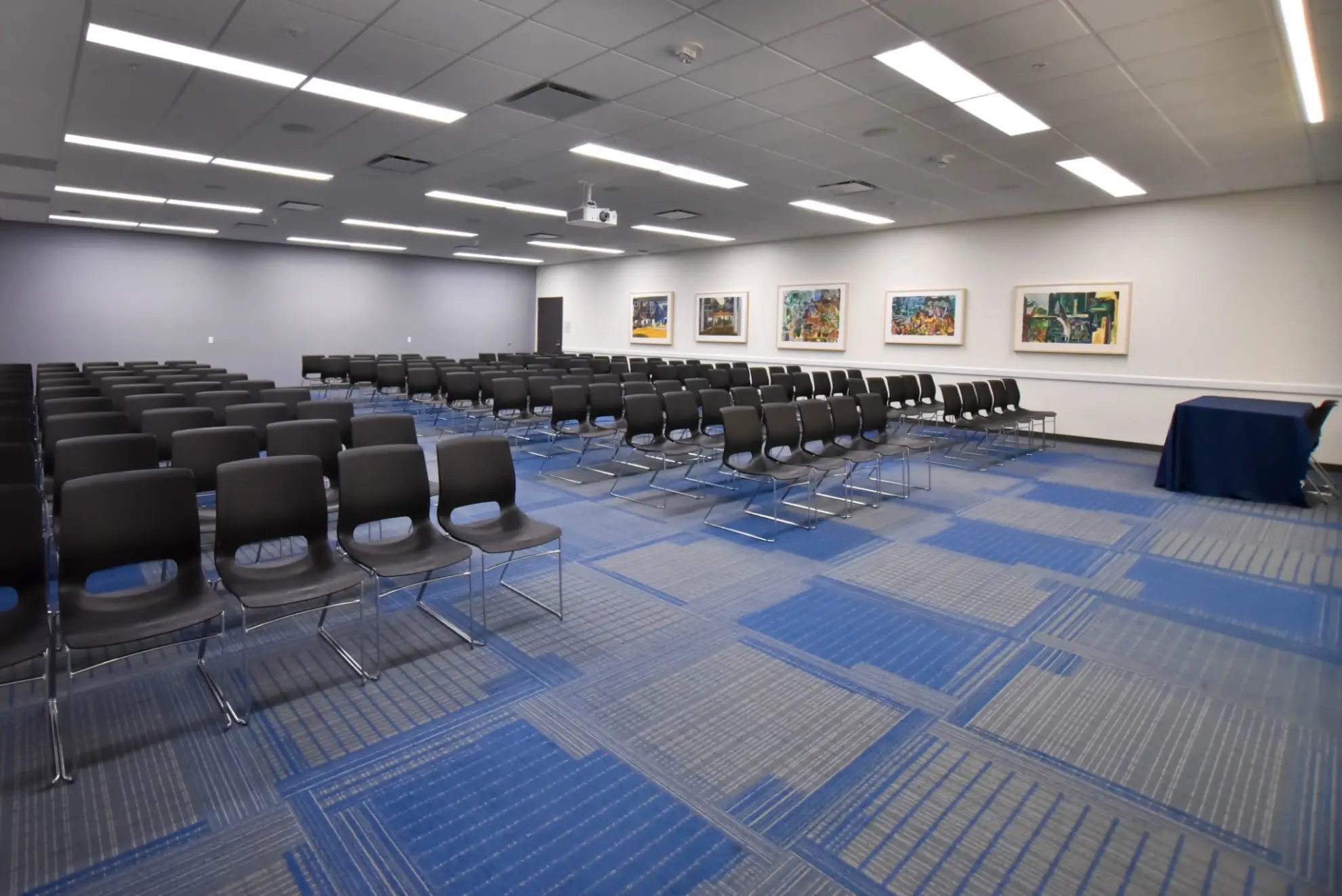 A large room with rows of empty chairs, a projector screen, and artwork on the walls.